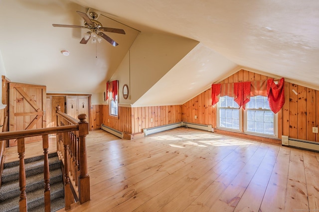 additional living space featuring wooden walls, light hardwood / wood-style floors, vaulted ceiling, and baseboard heating