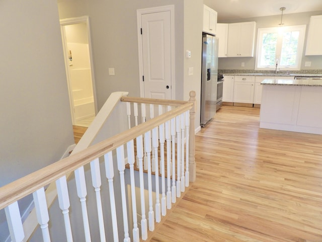 kitchen featuring appliances with stainless steel finishes, pendant lighting, sink, white cabinets, and light hardwood / wood-style flooring