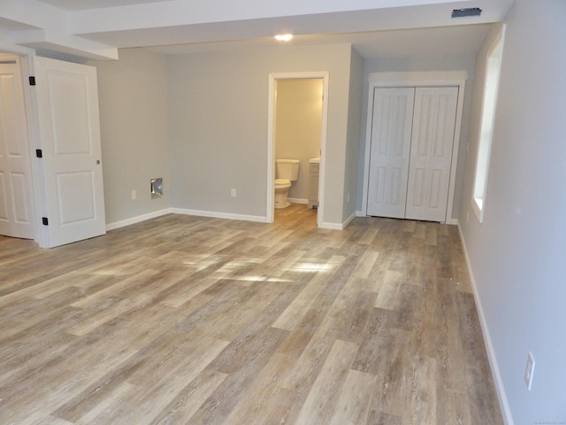 unfurnished bedroom featuring a closet, ensuite bathroom, and light hardwood / wood-style flooring