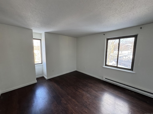 spare room featuring a baseboard radiator, dark hardwood / wood-style floors, a wealth of natural light, and a textured ceiling