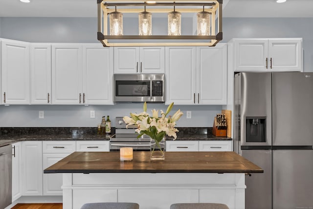 kitchen with white cabinetry, appliances with stainless steel finishes, butcher block counters, and decorative light fixtures