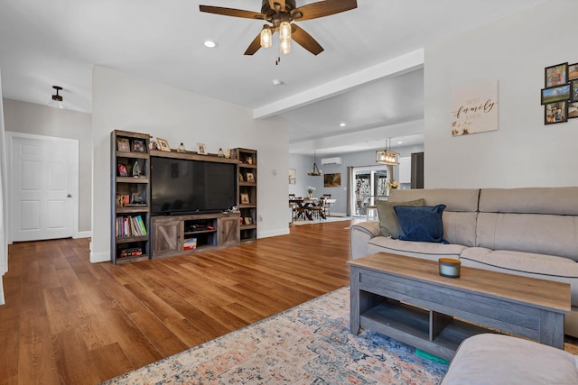 living room with ceiling fan with notable chandelier, beam ceiling, hardwood / wood-style floors, and a wall unit AC