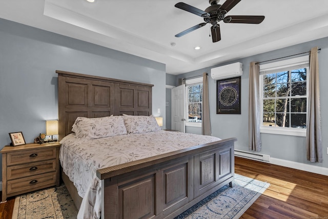 bedroom with ceiling fan, a tray ceiling, dark hardwood / wood-style flooring, a baseboard radiator, and an AC wall unit