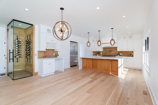 kitchen featuring white cabinets, decorative light fixtures, a spacious island, and built in refrigerator