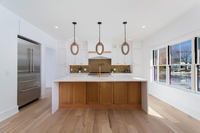 kitchen featuring white cabinetry, decorative backsplash, stainless steel built in fridge, a large island, and light wood-type flooring