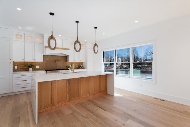 kitchen with tasteful backsplash, white cabinetry, pendant lighting, and a center island with sink