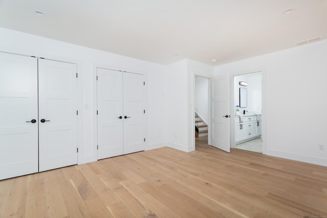 unfurnished bedroom featuring two closets, light hardwood / wood-style flooring, and ensuite bathroom