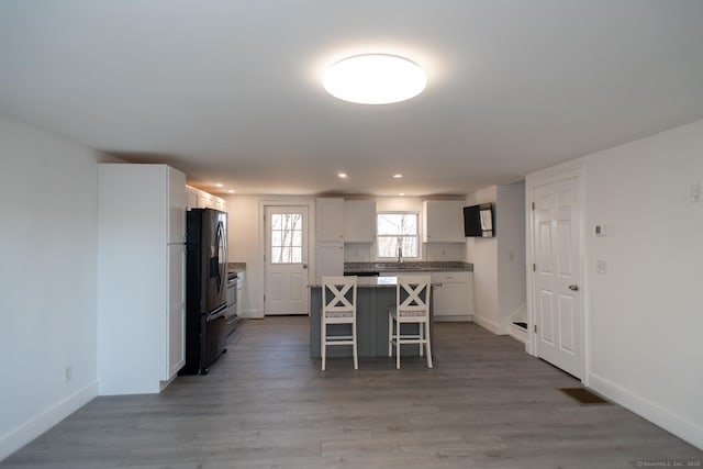 kitchen featuring white cabinetry, a kitchen breakfast bar, hardwood / wood-style flooring, a center island, and black fridge with ice dispenser