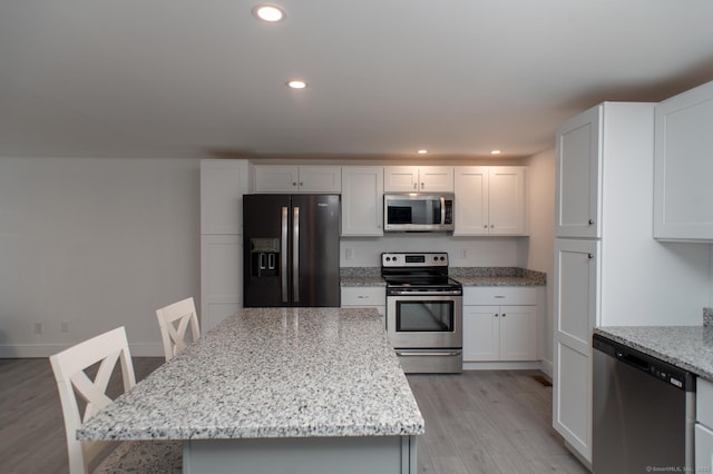 kitchen featuring light stone counters, white cabinetry, a kitchen island, and appliances with stainless steel finishes