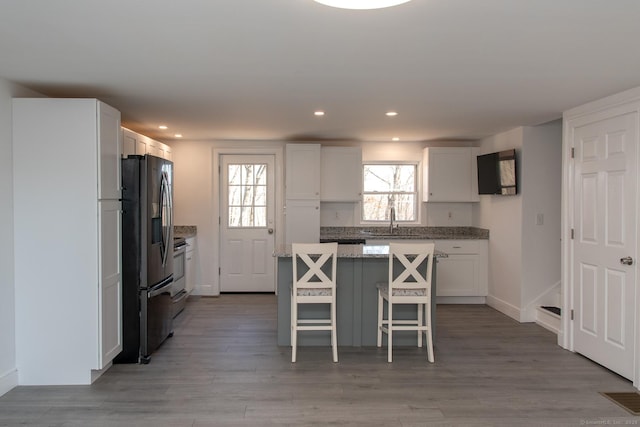 kitchen with black fridge with ice dispenser, sink, white cabinetry, a center island, and a kitchen breakfast bar