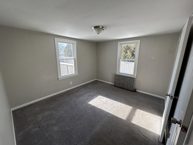 spare room featuring dark carpet, a wealth of natural light, and radiator heating unit