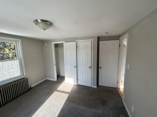 unfurnished bedroom with multiple closets, radiator, and dark carpet