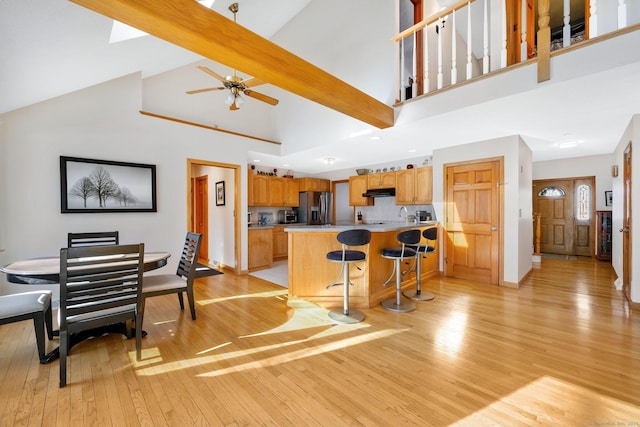 kitchen with stainless steel fridge, a breakfast bar area, high vaulted ceiling, light hardwood / wood-style floors, and beamed ceiling