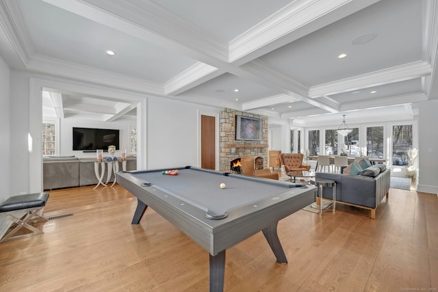 rec room with beam ceiling, light wood finished floors, pool table, a stone fireplace, and coffered ceiling