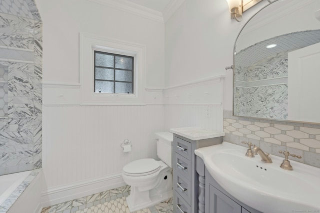 full bath with wainscoting, toilet, marble finish floor, crown molding, and vanity