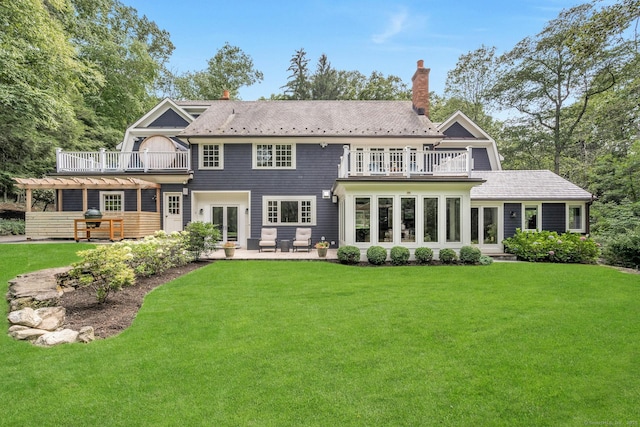 rear view of property featuring a yard, french doors, a chimney, and a balcony