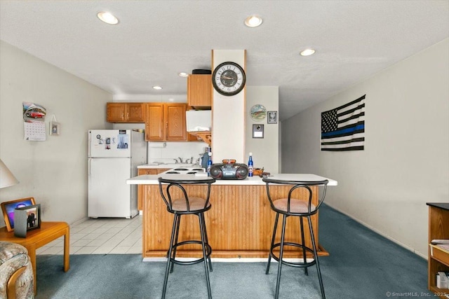 kitchen with light carpet, a breakfast bar, kitchen peninsula, and white fridge