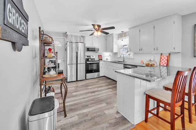 kitchen featuring white cabinetry, sink, dark stone countertops, kitchen peninsula, and stainless steel appliances