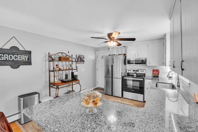 kitchen featuring sink, a baseboard heating unit, stainless steel appliances, light stone counters, and white cabinets