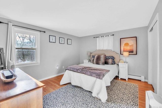 bedroom with a baseboard heating unit, light hardwood / wood-style floors, and a closet