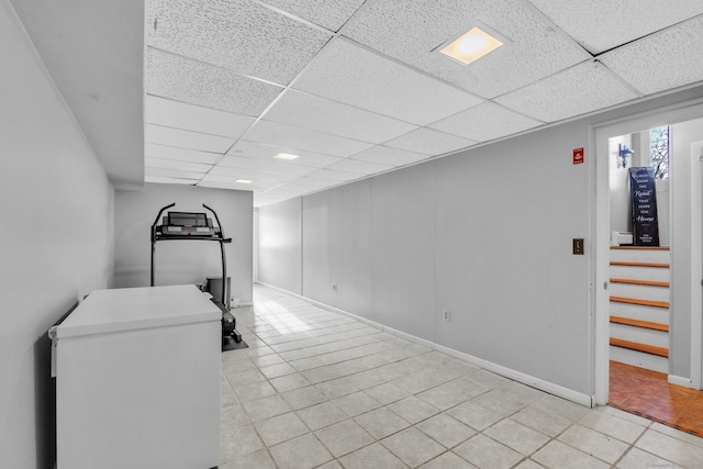 basement featuring light tile patterned flooring, fridge, and a drop ceiling