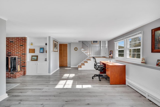 unfurnished office featuring a brick fireplace, light hardwood / wood-style floors, and a baseboard heating unit