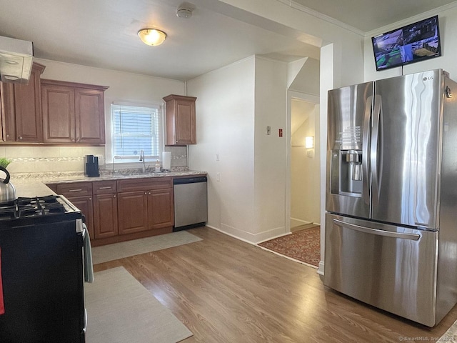 kitchen featuring appliances with stainless steel finishes, tasteful backsplash, sink, light hardwood / wood-style floors, and crown molding