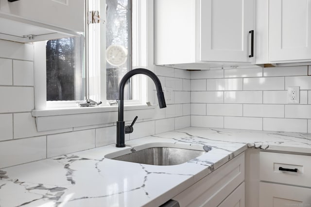 kitchen featuring tasteful backsplash, sink, light stone countertops, and white cabinets