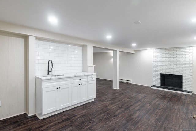 basement featuring a baseboard radiator, dark hardwood / wood-style flooring, sink, and a fireplace