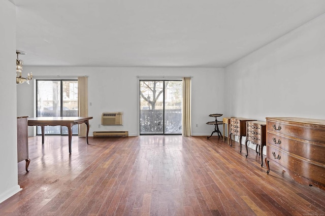 misc room with wood-type flooring, a baseboard heating unit, a wall mounted AC, and an inviting chandelier