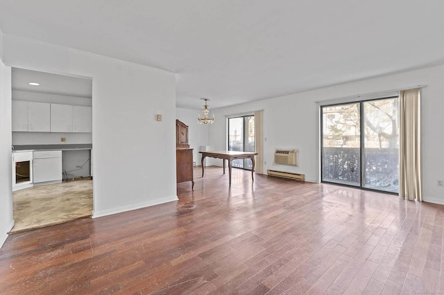 unfurnished room with hardwood / wood-style flooring, a baseboard radiator, a wall unit AC, and an inviting chandelier