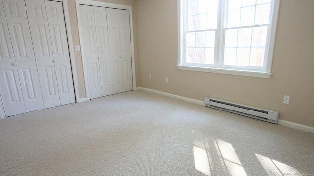 unfurnished bedroom featuring a baseboard radiator, light carpet, and two closets