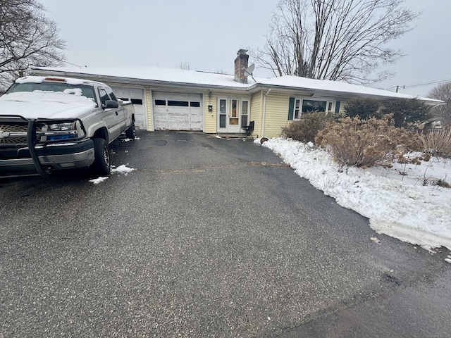 ranch-style home with an attached garage, a chimney, and aphalt driveway