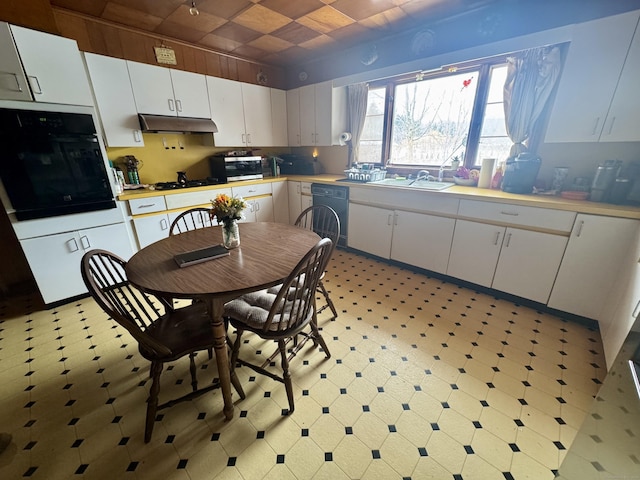 kitchen featuring light floors, under cabinet range hood, a sink, white cabinetry, and black appliances