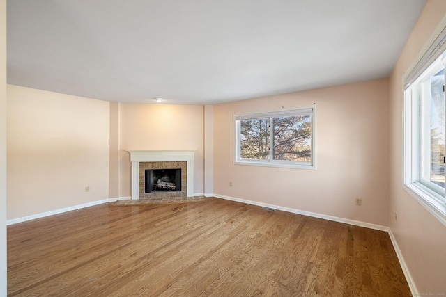 unfurnished living room with a tiled fireplace, hardwood / wood-style flooring, and a healthy amount of sunlight