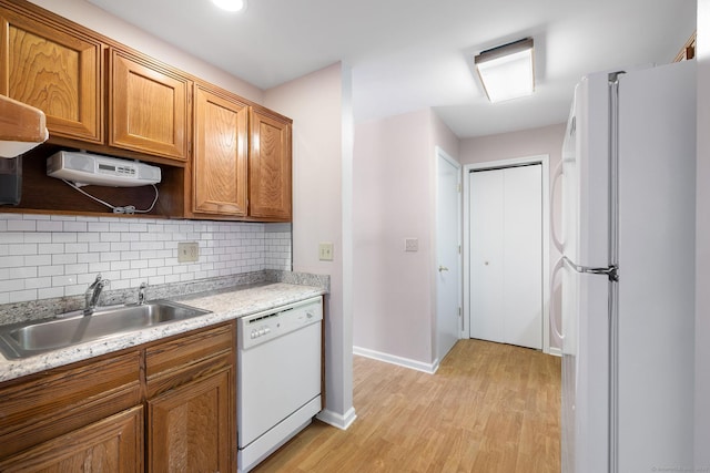 kitchen with sink, white appliances, light hardwood / wood-style floors, light stone countertops, and decorative backsplash