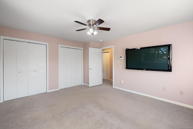 unfurnished bedroom featuring light carpet, two closets, and ceiling fan