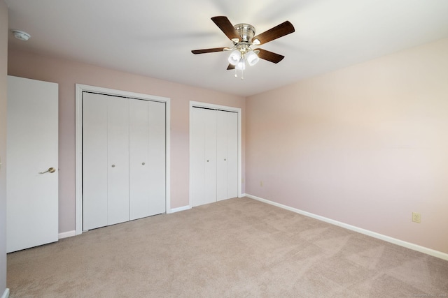 unfurnished bedroom with ceiling fan, light colored carpet, and two closets