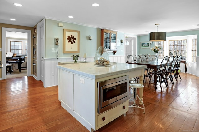 kitchen featuring white cabinetry, light hardwood / wood-style flooring, stainless steel microwave, ornamental molding, and pendant lighting