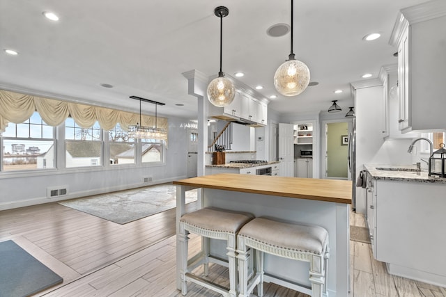 kitchen featuring a breakfast bar, butcher block counters, sink, white cabinets, and light hardwood / wood-style flooring