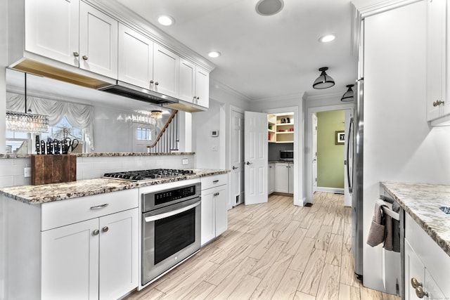 kitchen with light stone counters, tasteful backsplash, ornamental molding, appliances with stainless steel finishes, and white cabinets