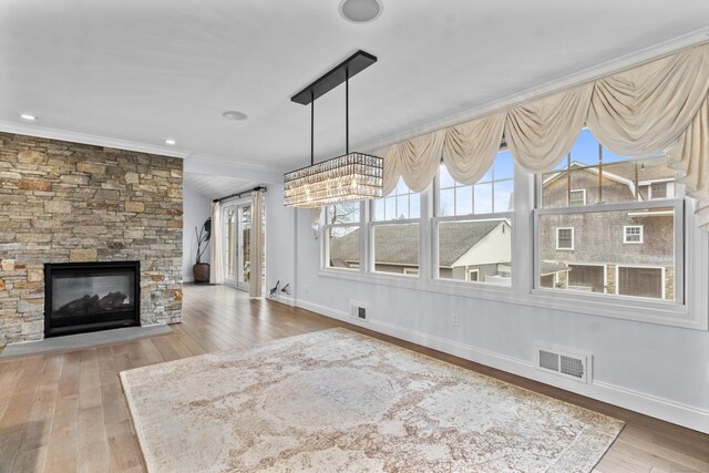 unfurnished living room with crown molding, hardwood / wood-style flooring, and a stone fireplace