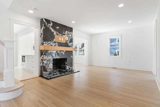 unfurnished living room with light hardwood / wood-style flooring, a high end fireplace, and decorative columns