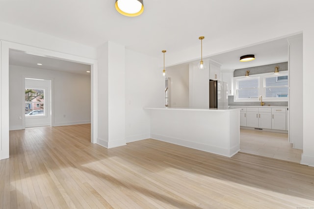 interior space with white cabinetry, white fridge, sink, and hanging light fixtures