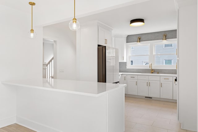 kitchen featuring fridge, pendant lighting, kitchen peninsula, and white cabinets