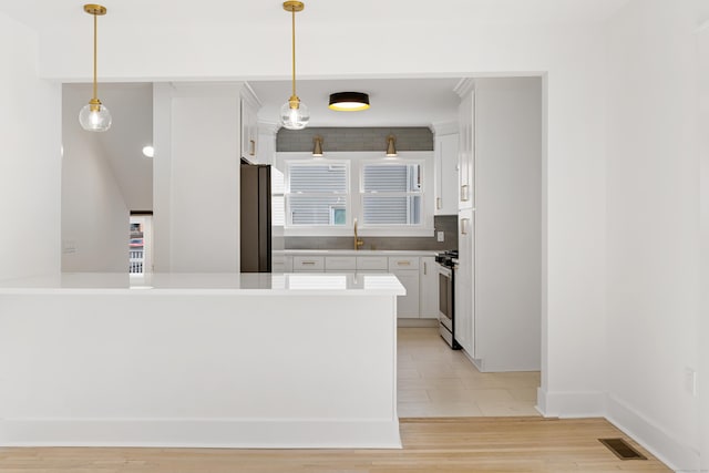 kitchen featuring sink, white cabinetry, decorative light fixtures, black refrigerator, and light hardwood / wood-style floors