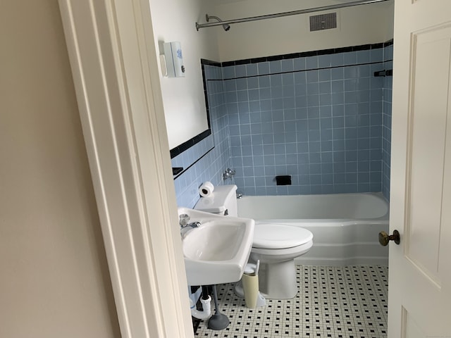 bathroom with tiled shower / bath, tile patterned floors, toilet, and tile walls