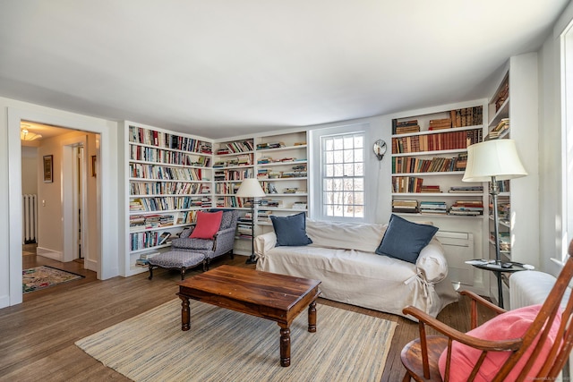 living area with radiator heating unit, built in shelves, and wood finished floors