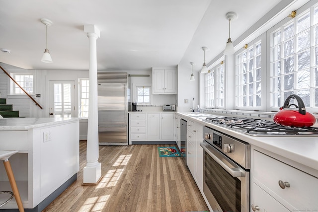 kitchen featuring decorative columns, stainless steel appliances, light countertops, hanging light fixtures, and light wood-type flooring