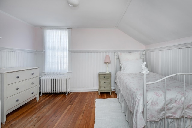 bedroom featuring radiator, wood-type flooring, vaulted ceiling, and wainscoting